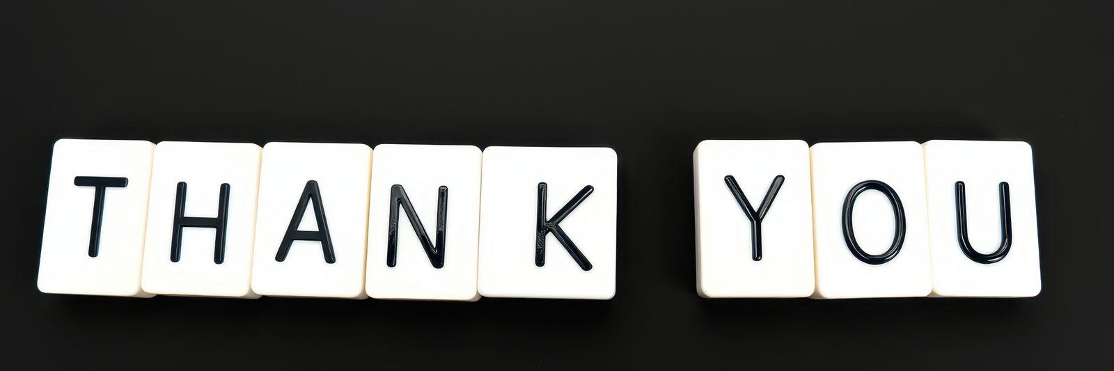 Expression of gratitude displayed through white letter tiles arranged on a black surface